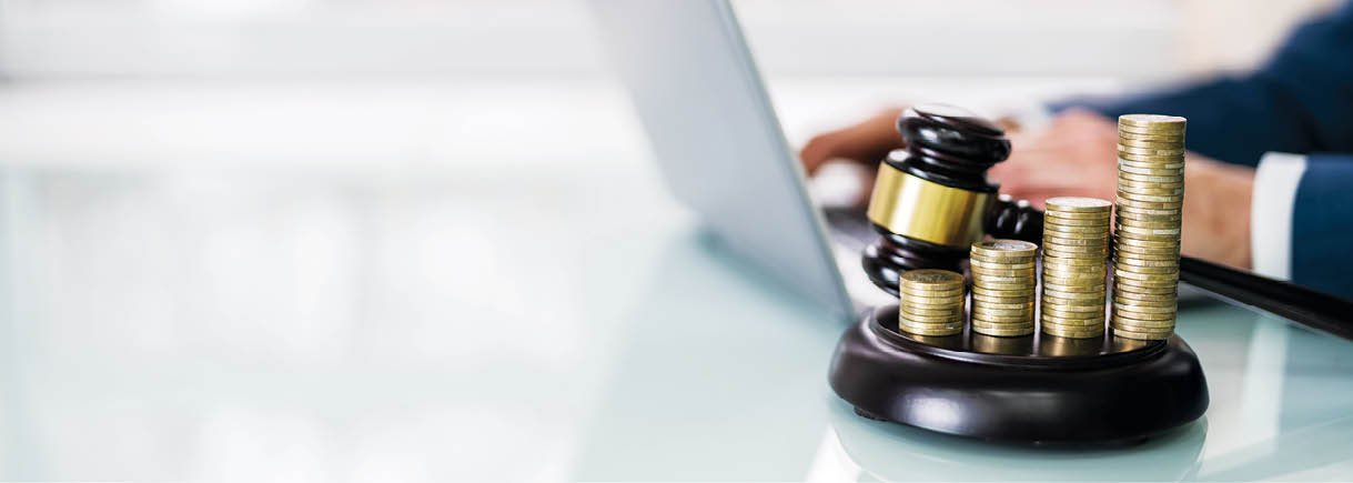 Judge Using Laptop Near Gavel And Stacked Coins In Courtroom