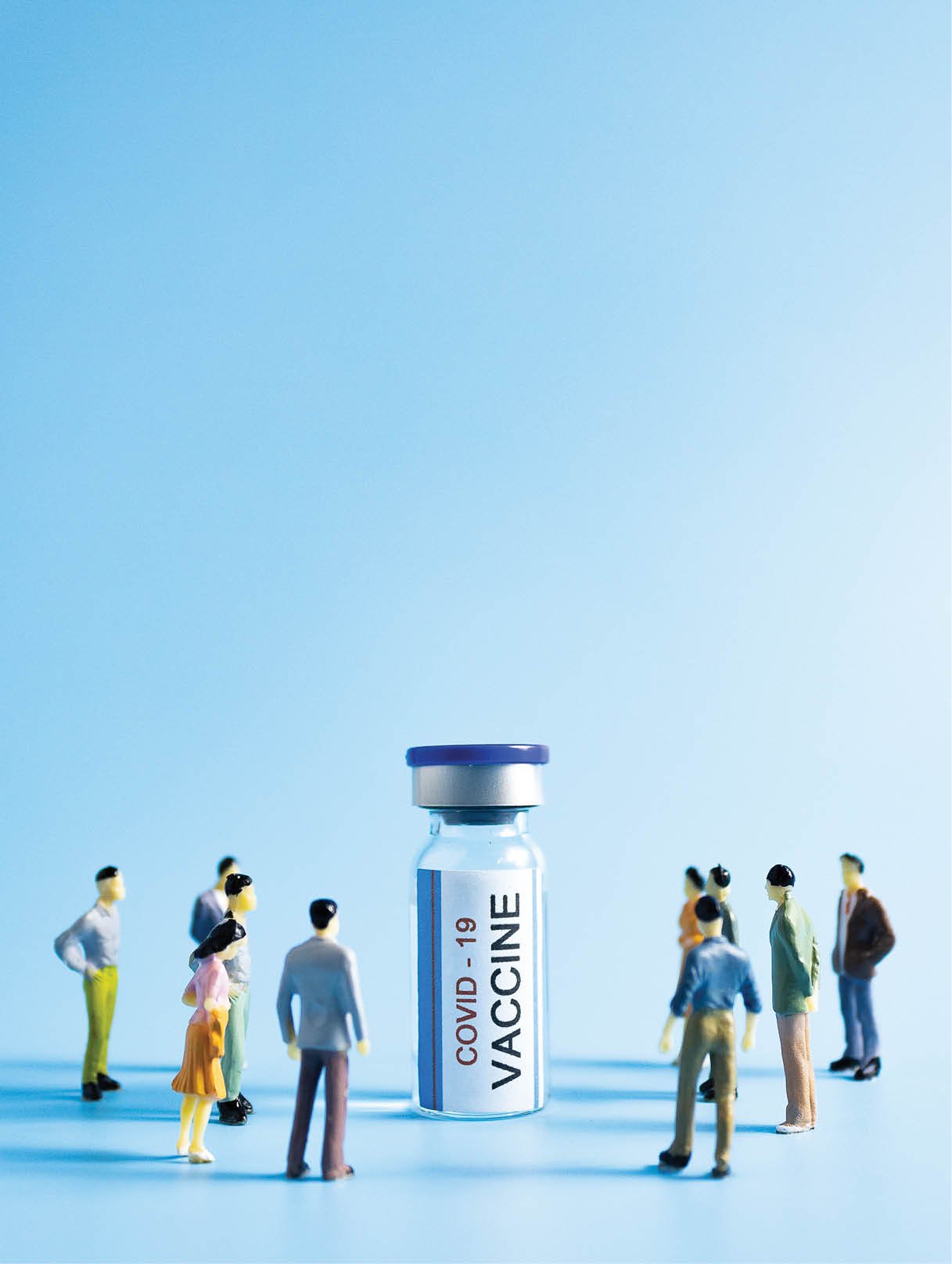 Miniature people surround a vial of Covid 19 vaccine  vaccination concept  vertical view  copy space 