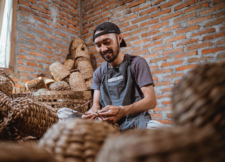 water hyacinth craftsman sitting weaving making souvenirs in a room full of woven baskets